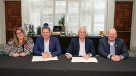 Picture of one woman and three men at a table signing a document