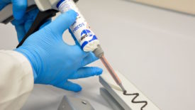 Picture of a gloved hand dispensing adhesive on a metal plate